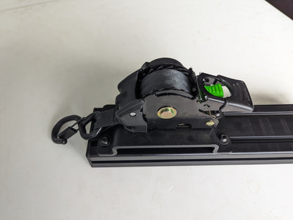 Rhino USA retractable ratchet strap and aluminum bracket bolted to a T-slot crossbar, angled view showing the strap hook and green release lever